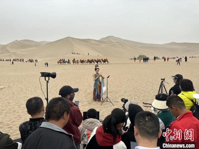圖為2023年4月底，敦煌大漠“逐舞者”奧楠在鳴沙山月牙泉景區(qū)視頻直播，吸引游人圍觀。　馮志軍 攝